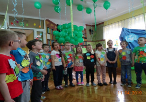 Zielone balony, chmurki oraz dzieci z naklejonymi na bluzkach liściami.recytujące wierszyk.